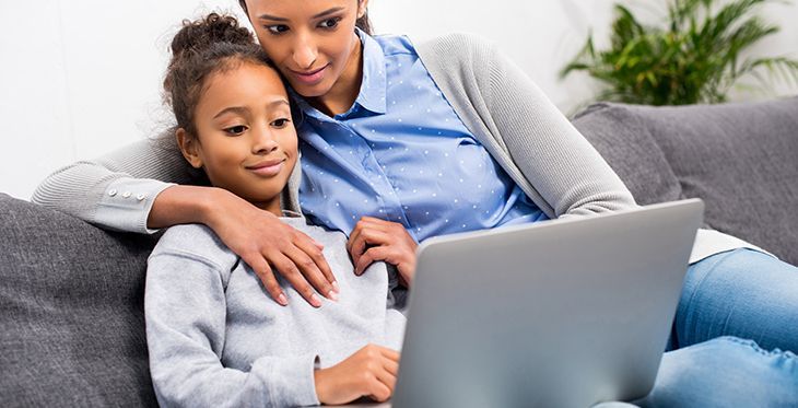 Mother and daughter looking at laptop on a couch, mother's arm around the girl.