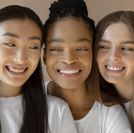 Three smiling women of different ethnicities posing together.