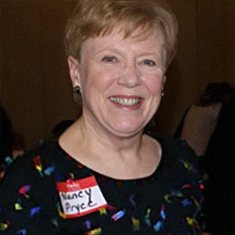 Woman with short blonde hair smiles, wearing a black top with colorful accents, name tag reads