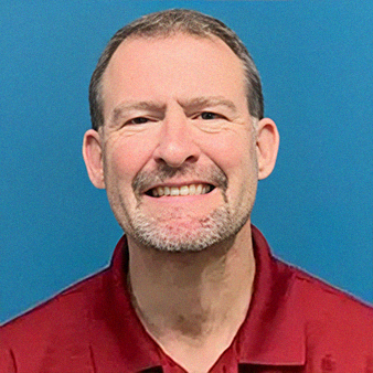 Man with a beard smiles, wearing a red polo shirt against a blue background.
