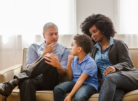 Family of three on a couch, the father is talking, while the boy and mother are listening.