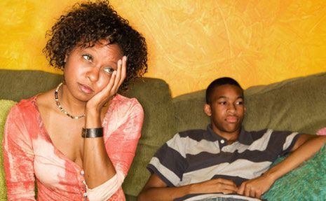 Woman with hand on cheek, looking weary, beside a teenage boy on a sofa.