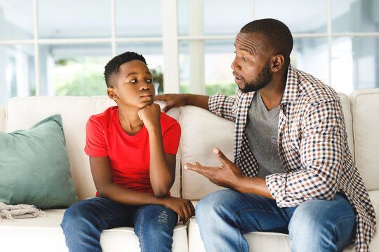 Father talking to his son on a couch; son looks pensive.