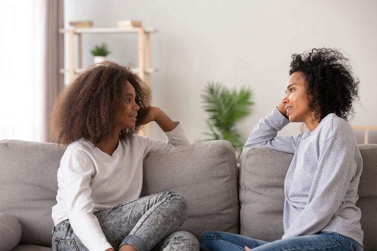 A Black woman and a girl talking on a couch in a living room.