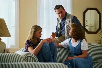 Family having a serious conversation on a striped sofa in a living room.