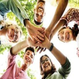 Group of smiling young people with hands together, celebrating teamwork outdoors.