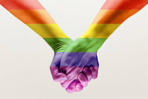 Two hands clasped together, painted with the rainbow Pride flag.