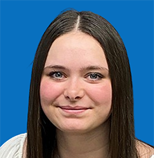 Young woman with brown hair and blue eyes smiles at the camera. Blue background.