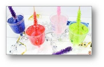 Four colorful rock candy sticks suspended in cups of sugary water.