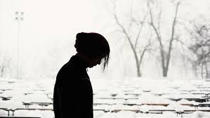 Silhouette of a person with head bowed, standing outside in snowy weather.