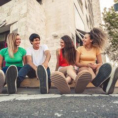 Four young adults sitting outdoors, smiling and laughing.