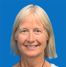 Woman with blonde hair, smiling, wearing white top, against a blue background.