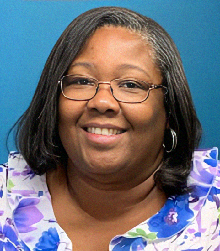 Woman with glasses smiling, wearing floral top, in front of a blue background.