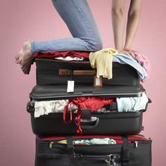 Person standing on three overflowing suitcases, struggling to close them.