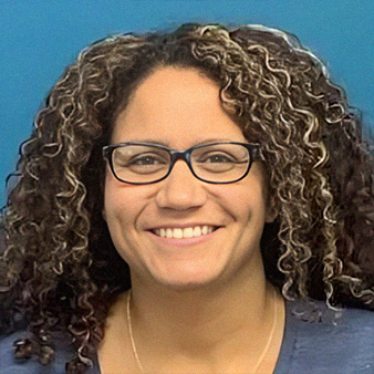 Woman with curly brown hair and glasses smiling in front of a blue background.