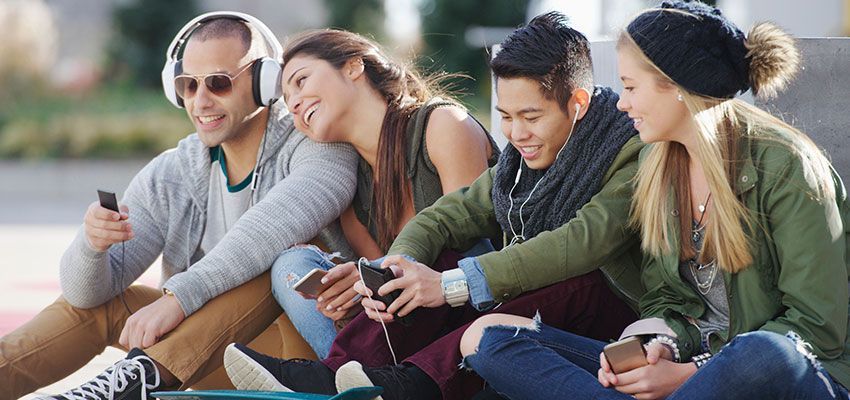 Four young people sitting outside, listening to music and looking at their phones.