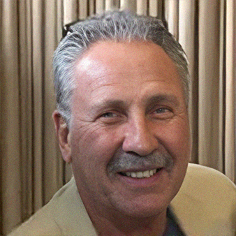 Smiling older man with gray hair, mustache, wearing a light jacket.