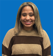 Young woman with brown hair and blue eyes smiles at the camera. Blue background.