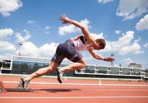 Sprinter in starting position on a red track, reaching forward against a blue sky.