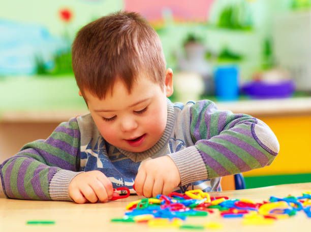 Young boy with Down syndrome plays with colorful toys at a table.