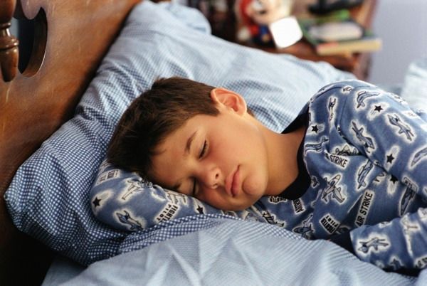 Boy asleep in bed, wearing blue pajamas, light blue sheets, setting is a bedroom.