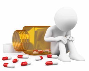 White figure sits dejectedly next to an overturned pill bottle and scattered capsules.