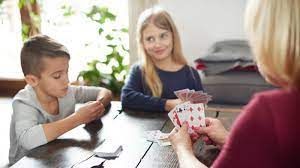 Boy and girl playing cards with a woman at a table in a home.