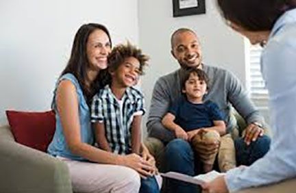Family of four smiling while consulting with a professional in a living room.
