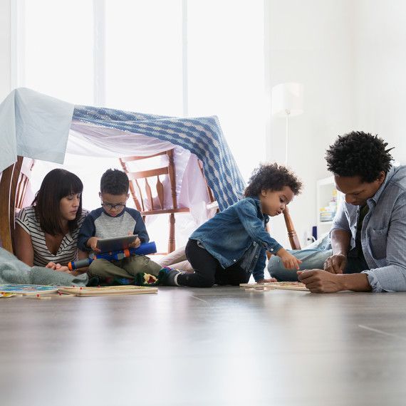 Family inside a blanket fort on the floor. Mother, father, and children play together.