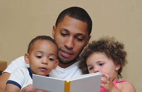 Man reads to two young children; all looking at a book together.