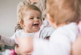 Smiling baby in a caregiver's arms; mirror reflection shows a similar baby.