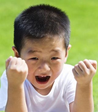 Boy with short black hair, clenching fists, and open mouth, celebrating outdoors on green grass.
