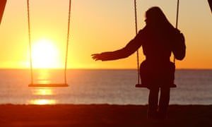 Silhouette of a person on a swing set near the ocean at sunset; arm reaching toward an empty swing.