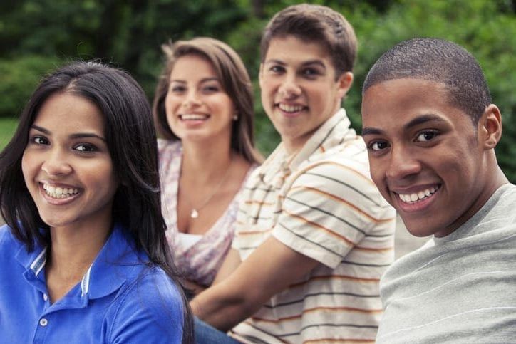 Four smiling diverse young adults posing outdoors.