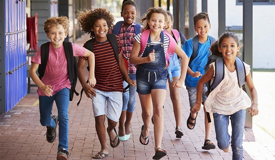 Group of diverse school children running and smiling down a hallway.