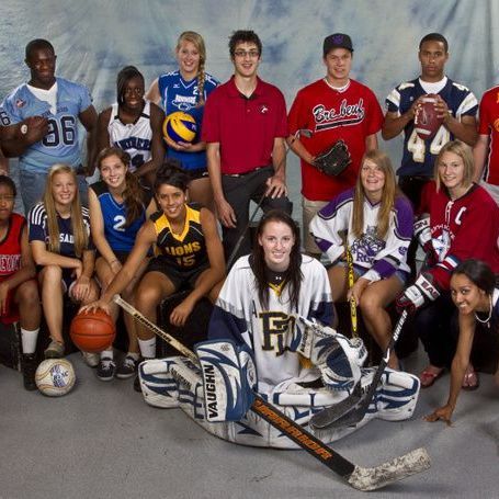Group of diverse athletes in various sports uniforms, smiling, posing for a photo.