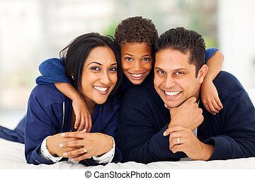 Happy family of three: mother, father, and son, smiling and embracing, lying on a bed.