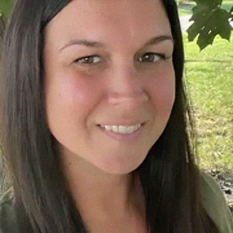 Woman with dark hair, smiling outdoors, green background.