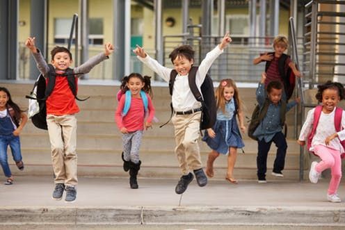 Group of elementary school children jumping happily outside the school.