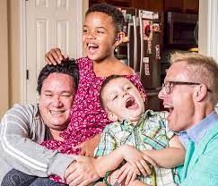 Two men with two laughing children in a home setting.
