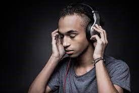 Young man with headphones listening intently, eyes closed, against a dark background.