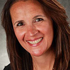 Woman with brown hair, smiling broadly, looking towards the viewer.