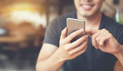 Man smiles while using a smartphone with his fingers, blurred background with natural light.