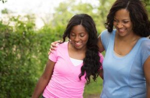 Woman and teen girl with arm around each other, smiling, walking outside.