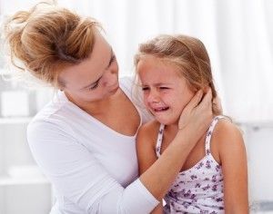 Woman comforting crying girl, indoors. Woman's hand on girl's face.