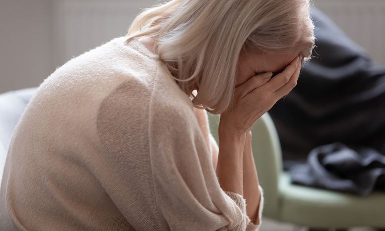 Woman with blonde hair, covering her face with her hands, possibly crying, indoors.