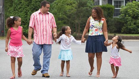 Family of five walking down a street, holding hands and smiling; sunny day.
