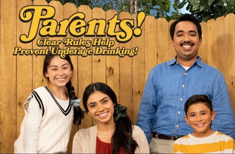 Family smiling in front of wooden fence. Text: