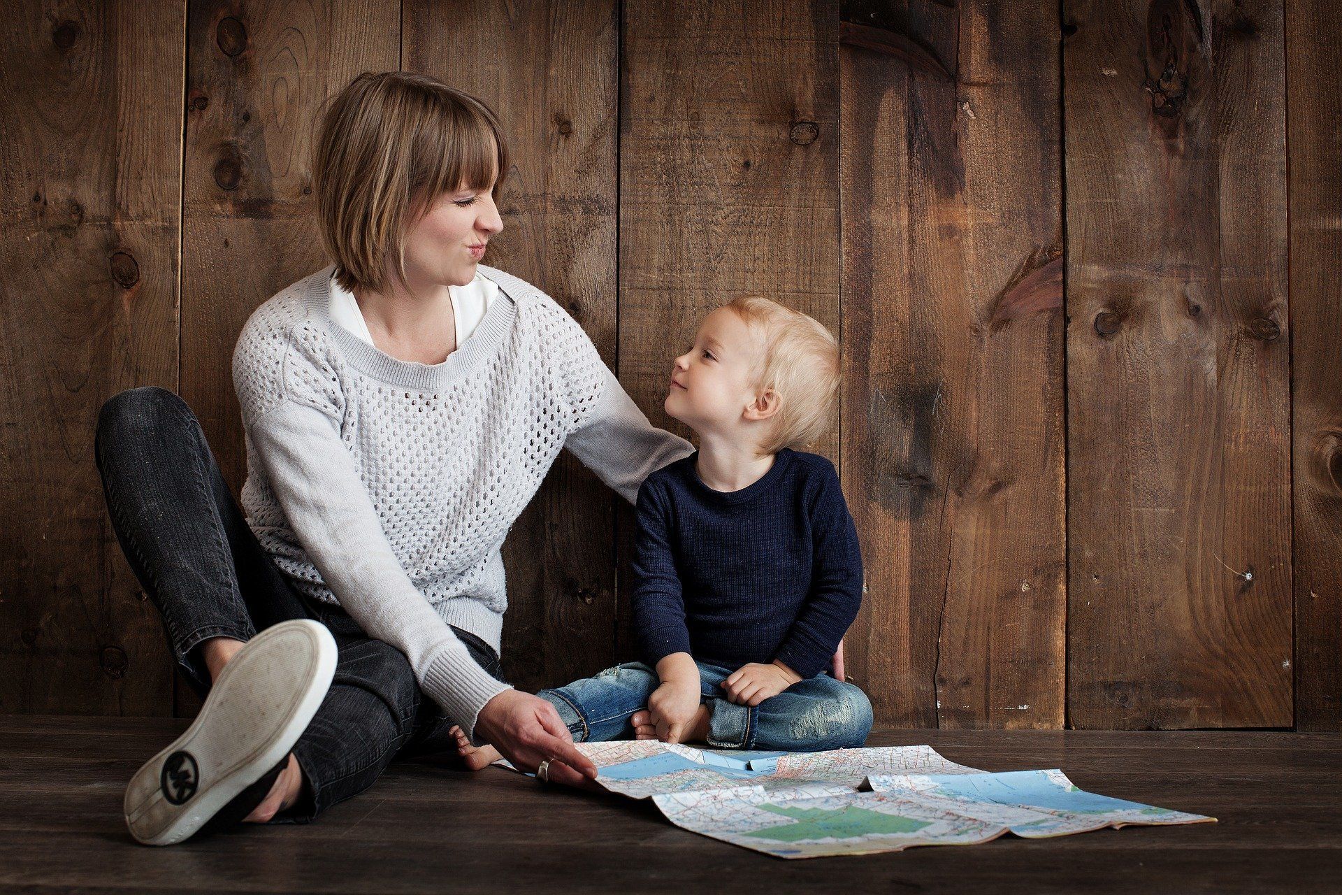 Woman and child looking at a map, sitting on the floor against a wooden wall.