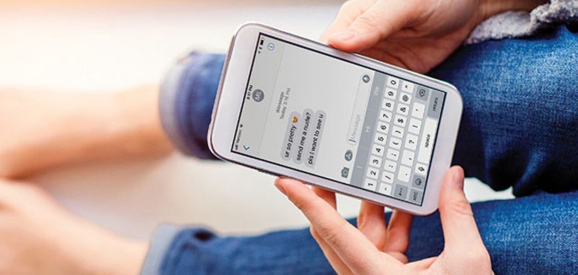 Person using a white smartphone, typing in a text message. They are wearing blue jeans, outdoors.